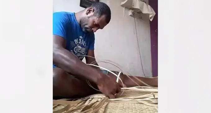 Kolinio Lesi weaves a mat at his home.