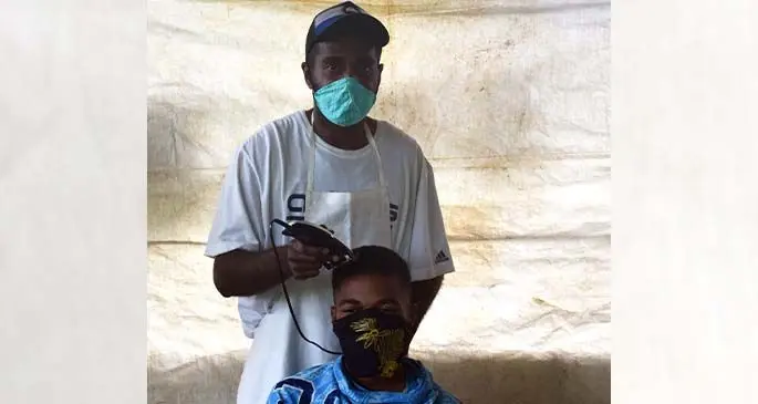 Timoci Notu cutting his customer’s hair at his home in Saunaka Village.