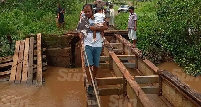 Nitya Nand holding his ten-month-old daughter, Nyla, crossing the damaged bridge in Soisoi, Labasa, on February 1, 2021. Photo: Shratika Naidu