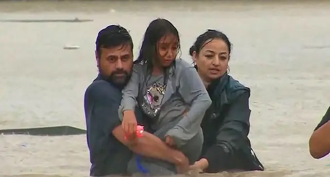 A family wades across waist-deep flood waters as weather forecast predicts more torrential rain for Auckland. Photo: RNZ Pacific