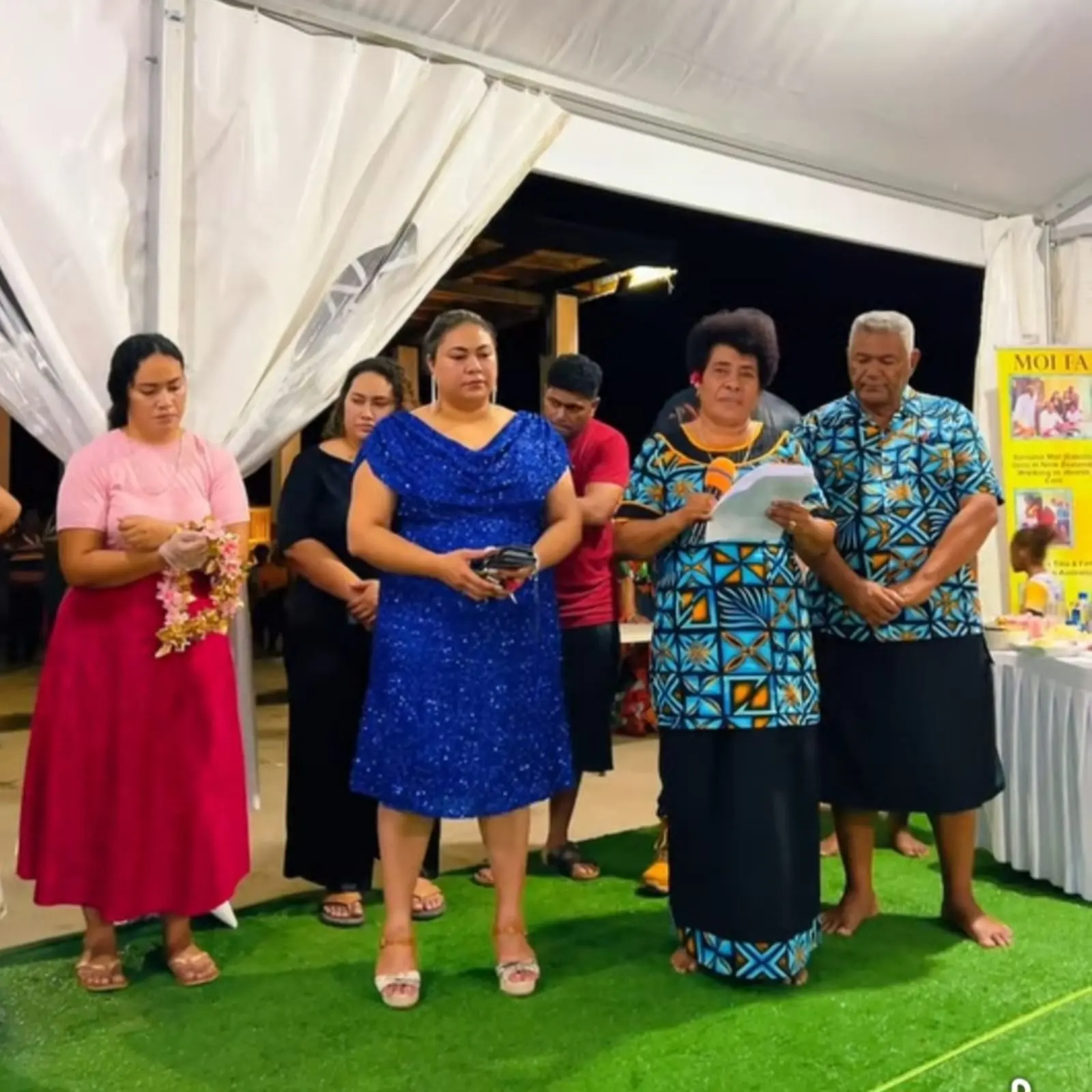 Maria Moi giving her speech alongside her husband, Reverend Peni Moi and their children.