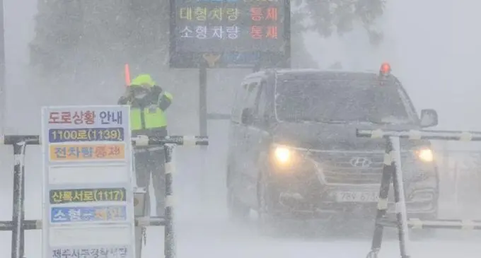 A police officer controls the entry of cars at a road on the southern resort island of Jeju amid heavy snowfall on January 24. Photo: The Korea Times