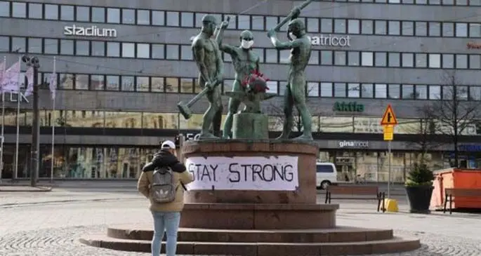 A citizen takes a picture of the famous city sculpture "Three Smiths" which has been put on facial masks, in Helsinki, Finland, March 31, 2020. (Xinhua/Zhu Haochen)