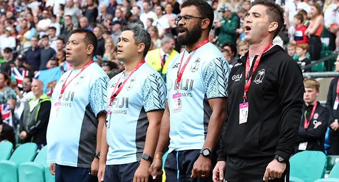 Fiji Airways Fijian 7s officials during the singing of the national anthem before the London 7s Cup final against Australia at Twickenham Stadium on May 27, 2019. From left: William Kwoong (physiotherapist), Kane Jury (assistant coach), Naca Cawanibuka (strength and conditioning coach) and head coach Gareth Baber, Photo:  World Rugby