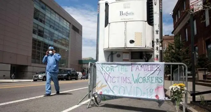 A healthcare worker walks past a memorial for COVID-19 victims in front of a refrigerated temporary morgue outside Brooklyn Hospital Center during the coronavirus pandemic in the Brooklyn borough of New York, the United States, on April 14, 2020. (Photo by Michael Nagle/Xinhua)