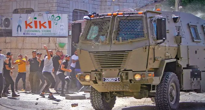 Palestinian youths throw stones at an armoured Israel Defence Forces vehicle during a raid on the West Bank on February 23. Photo: Israel Times 