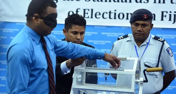 Supervisor of Elections Mohammed Saneem (second from left), supports the arm of a blindfolded man towards the box to draw a number on Monday, May 15, 2017. Photo: Jone Luvenitoga